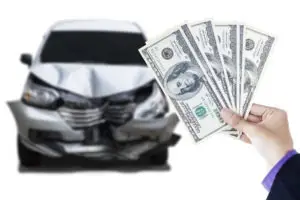 hand holding fanned hundred-dollar bills against damaged car