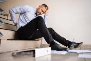 man sitting on stairs holding back and head after fall
