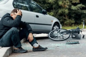 A driver sits on the curb after a car accident involving a bicycle. Distracted driving is one of the top reasons for crash crashes in South Dakota. A lawyer can help you recover damages if you got hurt in an accident.