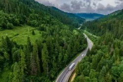 Trucks travel down a winding road on a forested interstate