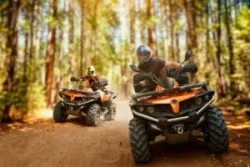 Two ATV riders race down a wooded track.