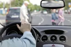 a driver’s hand is on the steering wheel as they approach three people walking in a crosswalk