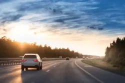 A white car drives on the highway at sunset.