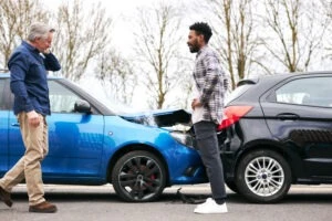 Two men stand on the road near their damaged vehicles after a rear-end accident