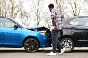 Man stands in the road and looks at damaged vehicle after rear-end accident