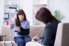 A woman with a crutch and her arm in a sling speaking with an experienced head-on collision lawyer in Miami.