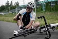 An injured cyclist holding his ankle and calling 911 at the scene of a bicycle accident.