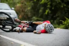 An injured cyclist lies on the road after being hit by a driver. A bicycle accident lawyer will help him get a settlement amount higher than the average.