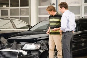 A claims adjuster assesses the damage to the front of a black car, and the accident victim wonders what the average car accident settlement is.