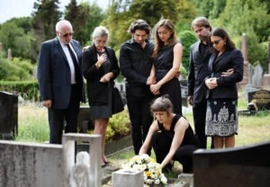 A family stands by the grave of a loved one after a funeral, placing flowers on the headstone, and wonders if you can sue for wrongful death after a motorcycle accident. ImageLink