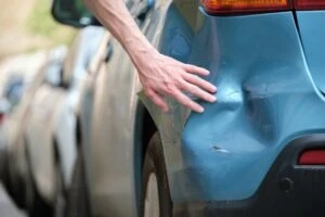 Driver’s hand examines bumper dent after minor Florida car accident.