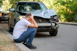 Man sitting in front of crashed car wondering average payout for a head-on collision