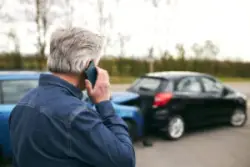 A man on a cell phone looking at two cars in an accident.