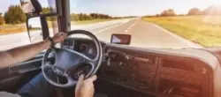 A truck driver with his hands on the steering wheel as he drives the open road.