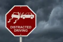 A sign on the road that says distracted driving with a car colliding with another due to not paying attention