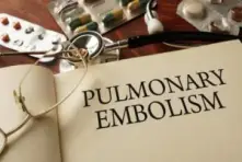 A book with the words "pulmonary embolism" printed on the page surrounded by medications and reading glasses