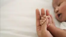 A newborn holds her mother’s hand