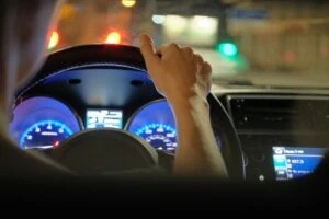 Close up of driver hands holding steering wheel driving car with blurred city street lights on background at night