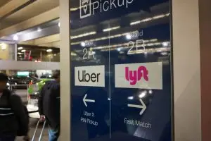 A sign has both the Uber and Lyft logos with arrows showing where pick-up areas are.