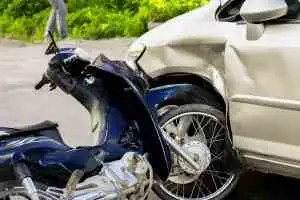 The aftermath of a motorcycle accident. Both the car and the motorcycle lie near each other damaged.