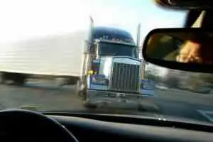 A tractor-trailer is about to hit another car from the point of view of the passenger vehicle.