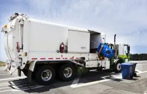 A garbage truck uses its hydraulic arm to collect trash from a bin on the sidewalk.