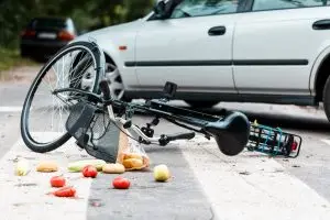 crashed bike with spilled groceries on street near car