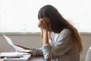 A woman holds her head in frustration as she struggles with paperwork.