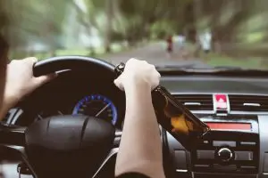 A woman speeds in a car while drinking behind the wheel.