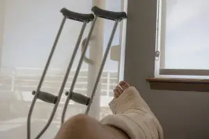 A disabled and injured man lying on the couch with his crutches on the wall.