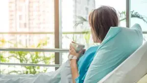 female patient in hospital bed with mug of tea