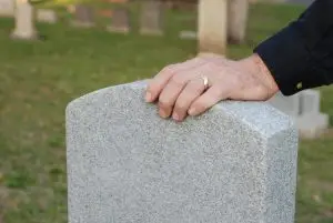 man rests hand on loved one’s gravestone
