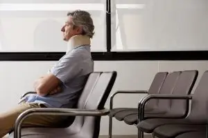 man with neck brace waits in hospital lobby