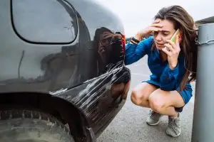 distressed woman standing near scratched car