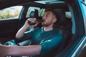 man drinking behind wheel of car