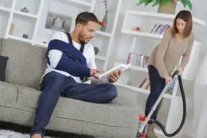 man with a broken arm while wife vacuums