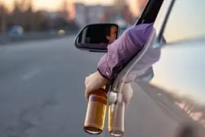 man’s arm hanging out of car with a beer