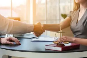 a male bus accident lawyer shaking hands with a female client who is seated at his desk.