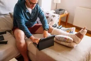 A bus accident victim with his leg in a cast is on a couch using a tablet.