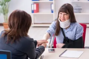 A woman wearing a neck brace and arm sling is consulting with a female attorney.