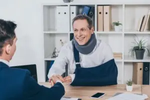 a man with a neck injury and broken arm shaking hands with a male attorney
