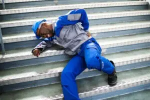 a male worker in a blue hard hat is lying on the stairs after falling