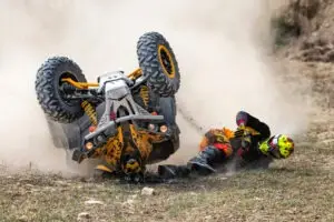 an ATV accident victim on the ground next to an upside-down quad