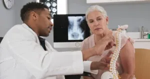 A doctor reviews a spinal column model with a patient. Epidural steroid injections that treat back pain can impact personal injury settlements.