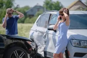 Woman leans against totaled car and asks lawyer on phone if total loss value of car is negotiable.