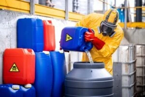 A worker in a yellow protective suit pours dangerous chemicals and risks a chemical exposure