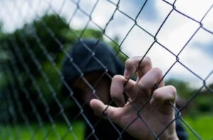 Teenage boy holding wired fence around a detention center while wondering how to file a juvenile detention center sexual abuse claim.