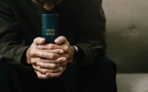 A faceless religious figure holds a Bible.