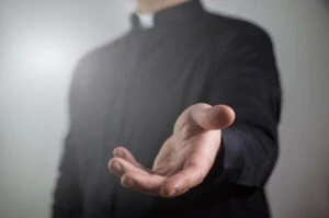 A priest holds out his hand to showcase a sign of clergy abuse