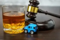 A gavel and a full whiskey glass next to a miniature car on a desk.